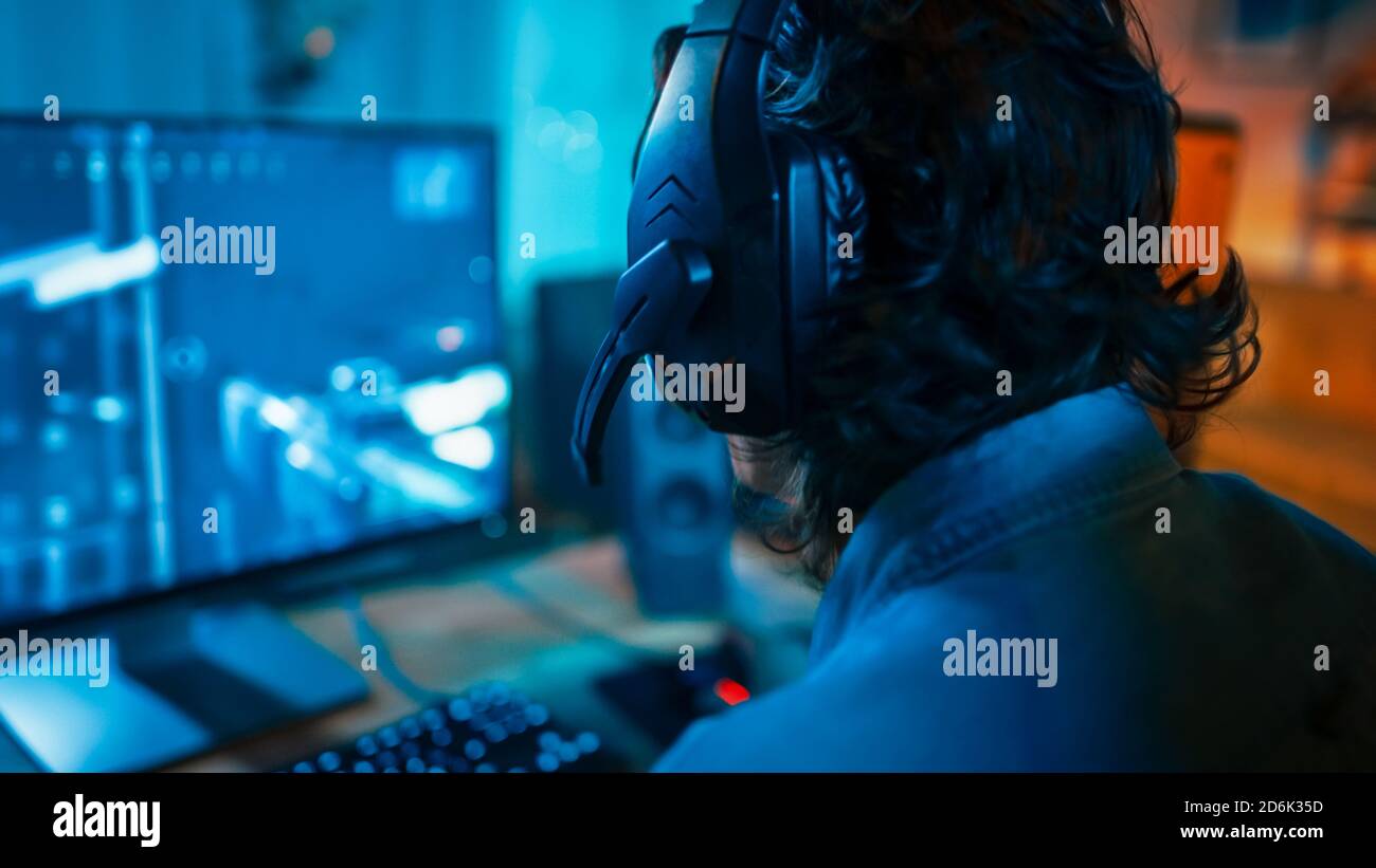 Primo piano Back Shot di un giocatore che indossa una cuffia con microfono e che gioca Online Shooter Video Game sul suo Personal computer. La camera e il PC sono colorati Foto Stock