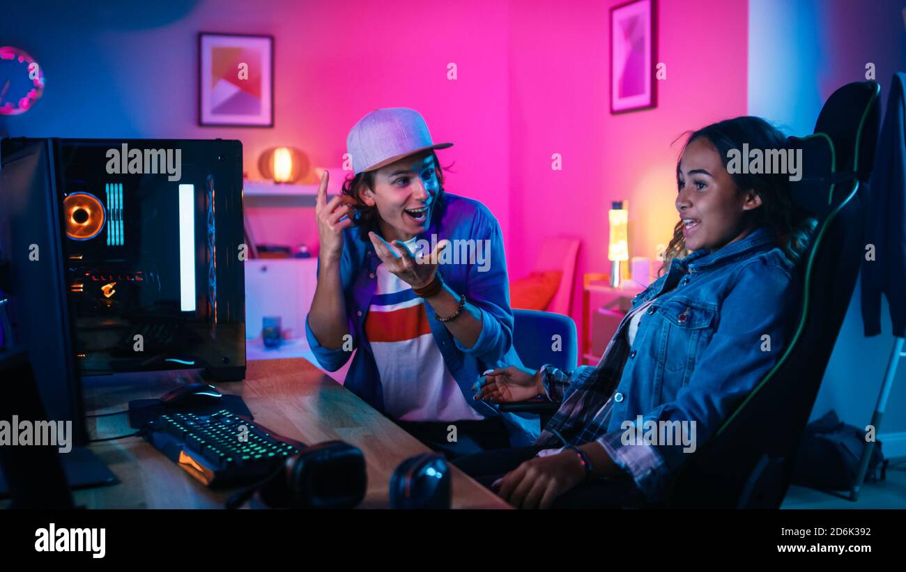 Young Man e Girl sorpresi ed eccitati guardano un Action Video su un potente Personal computer. Sono attivamente gesturing. Camera e PC hanno Foto Stock