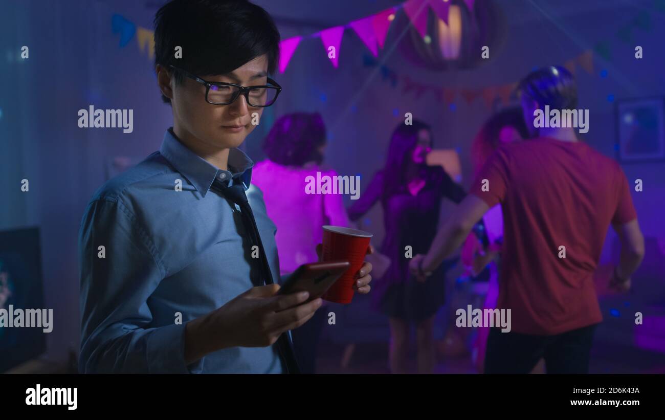 Al Wild House Party: L'uomo asiatico sicuro usa lo smartphone invece di ballare con altre persone. Foto Stock