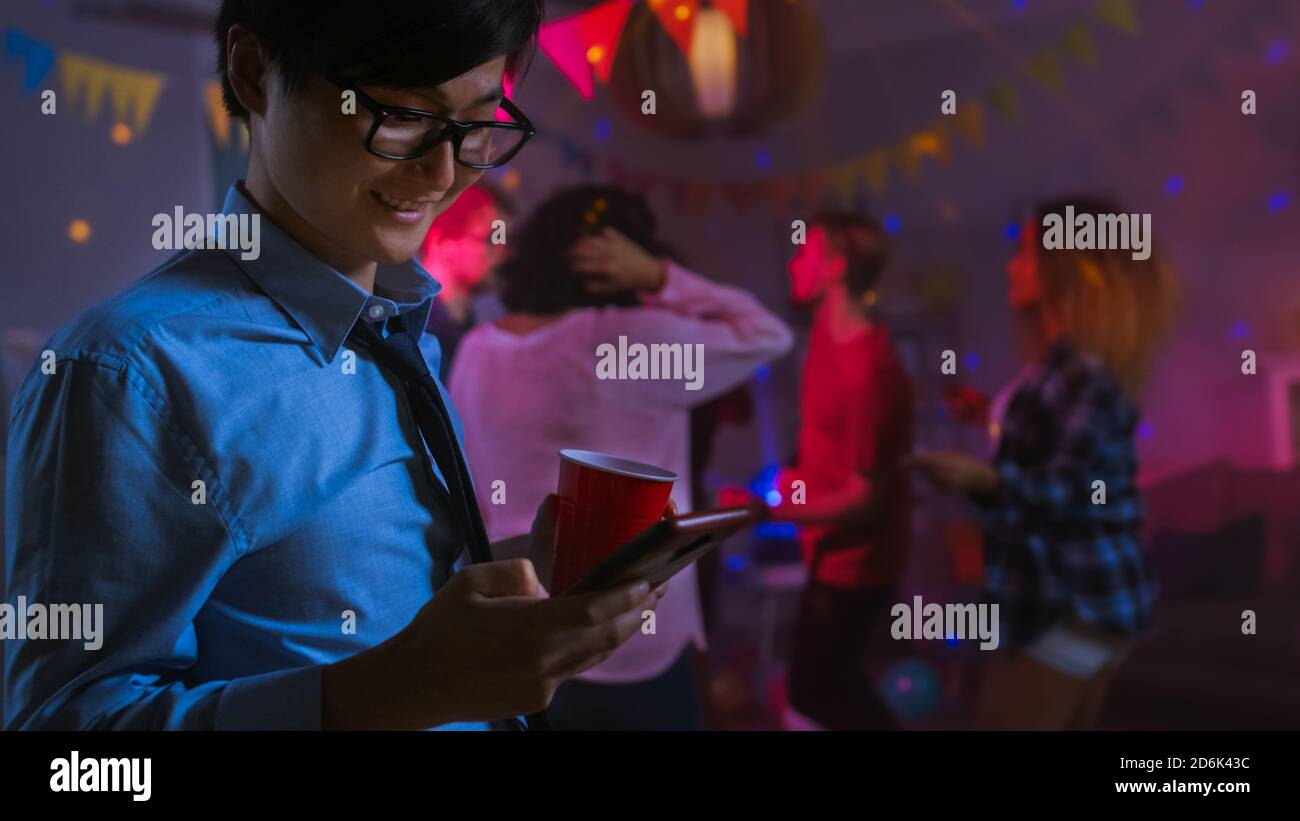 Al Wild House Party: Happy Asian Man utilizza smartphone invece di ballare con altre persone. Foto Stock