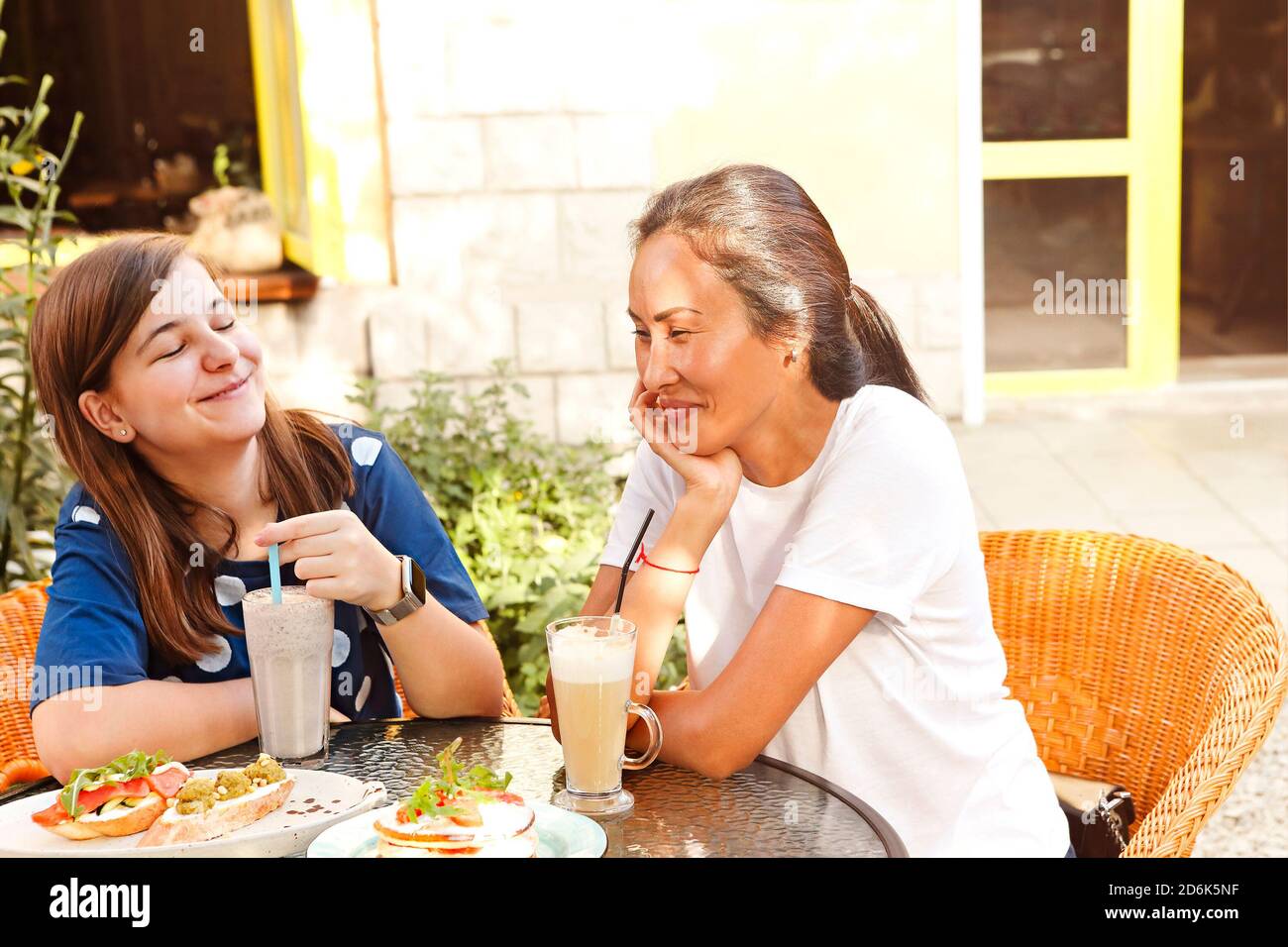 Felice giovane donna multirazziale amici seduti a tavola con panini e bevande fredde sulla terrazza del caffè durante l'orario di pranzo Foto Stock