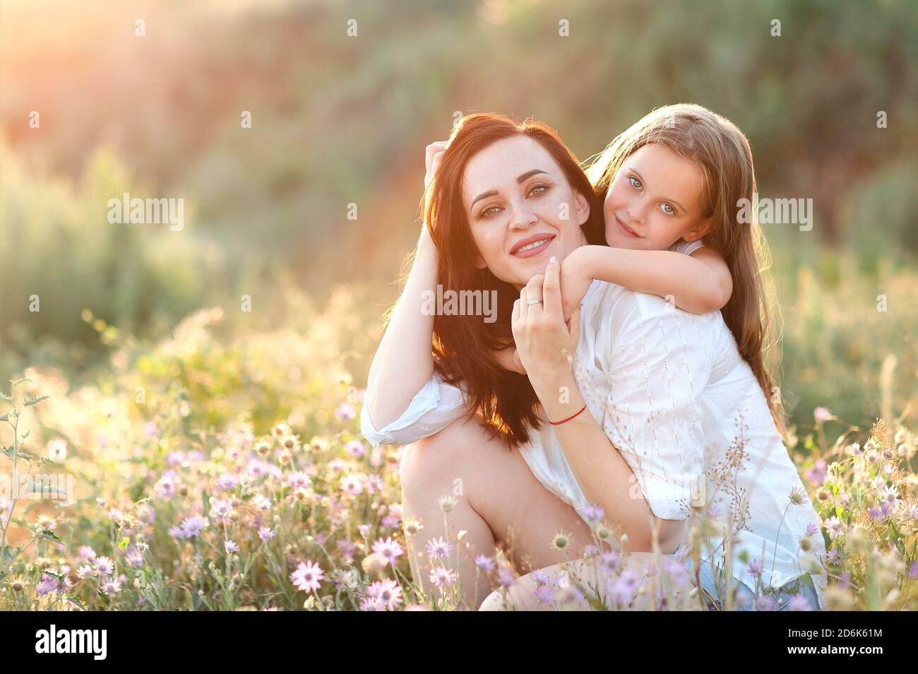 Sorridi madre e figlia coccolandosi dolcemente nel prato fiorente mentre trascorrete un fine settimana insieme in campagna e guardate la macchina fotografica Foto Stock