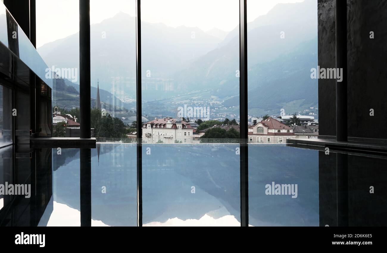 Vista degli edifici di Merano, del Tirolo del Sud e delle Alpi Italiane, delle montagne dall'interno di una lussuosa piscina interna. Foto Stock