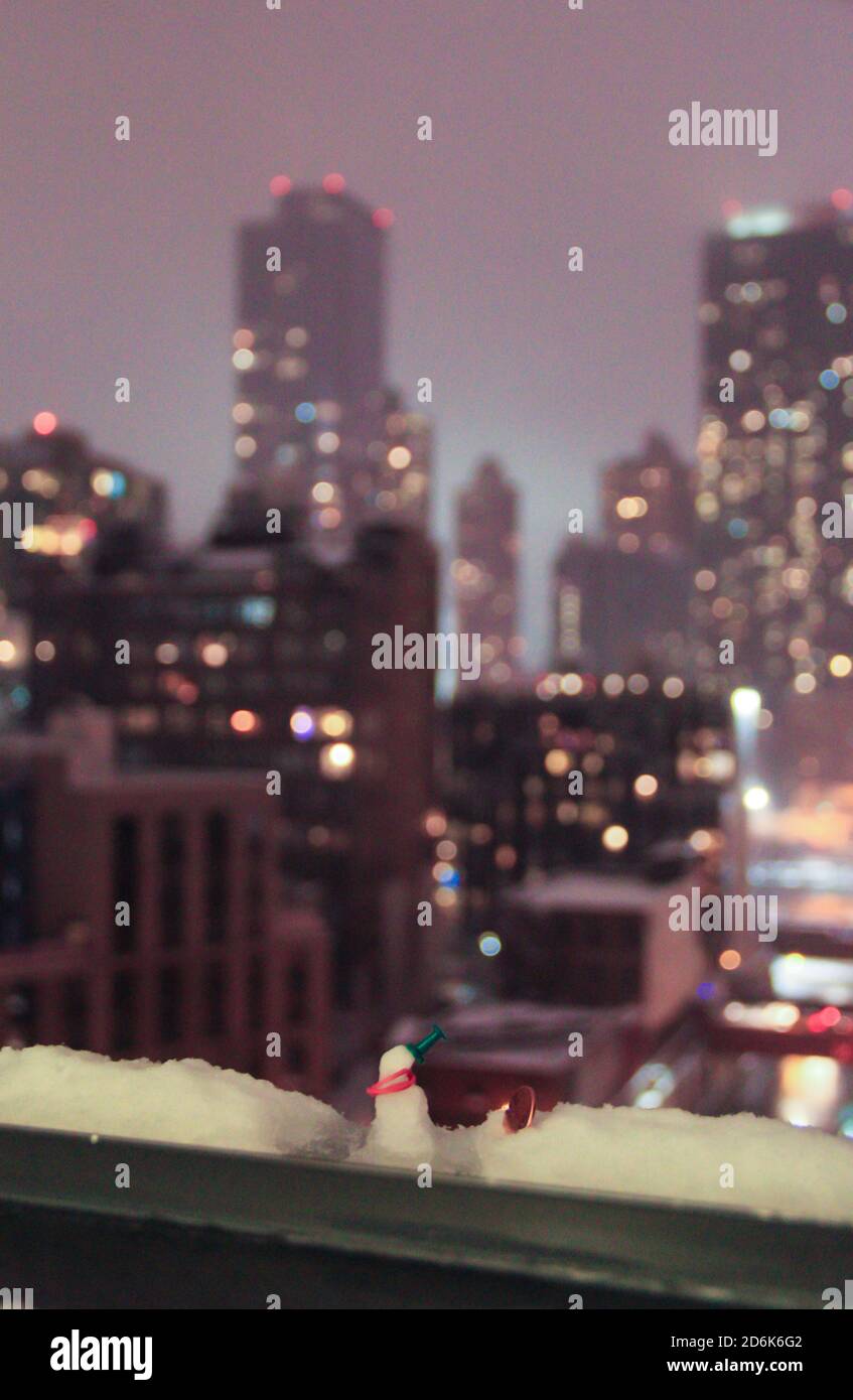 bokeh luci grattacieli città di new york con uomo neve in miniatura sul davanzale whimsical nevoso notte tempo Foto Stock