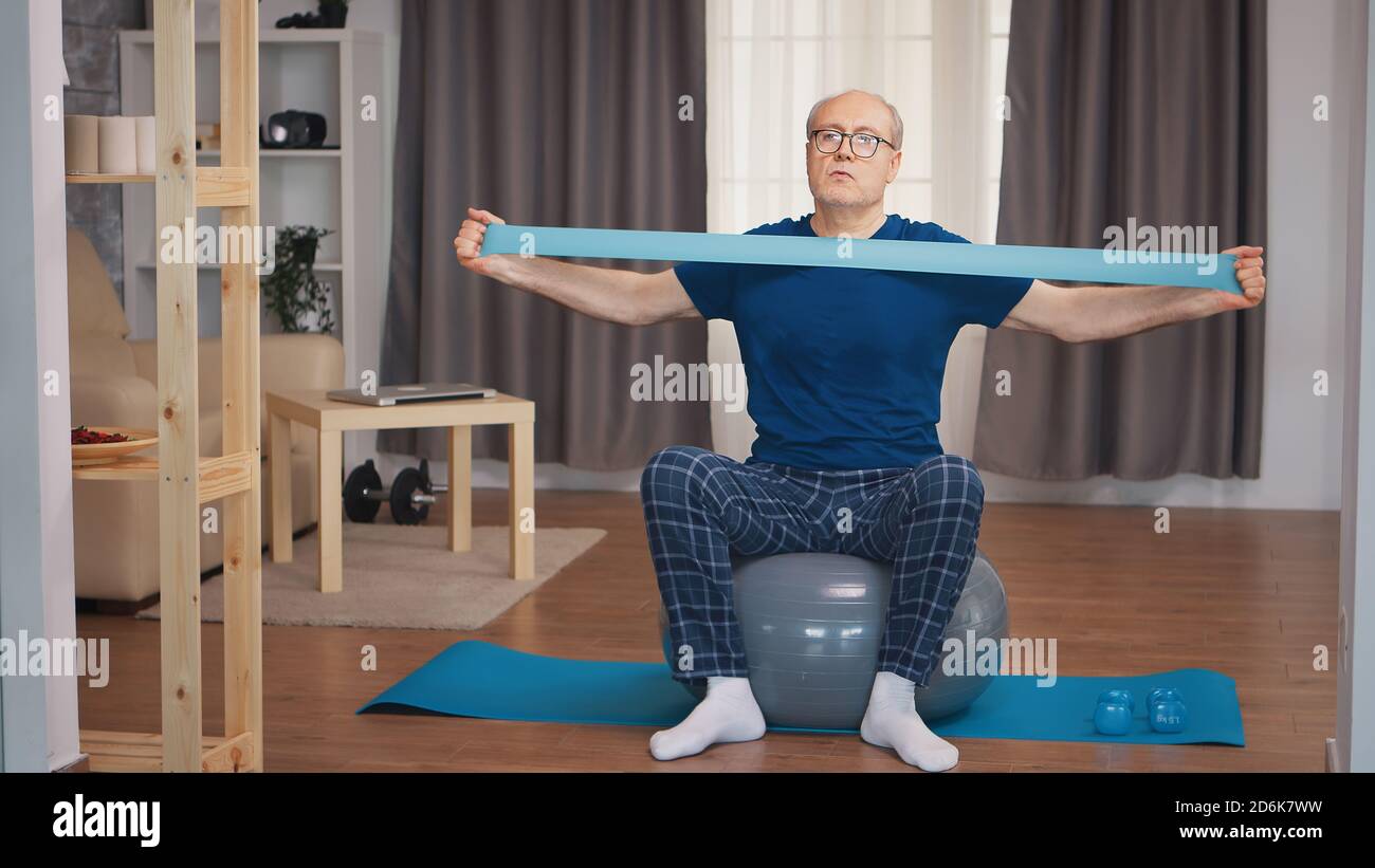 Uomo anziano in sport indossare esercizio con banda di resistenza. Anziano pensionato sano addestrando sport di salute a casa, esercitandosi attività di idoneità all'età anziana Foto Stock