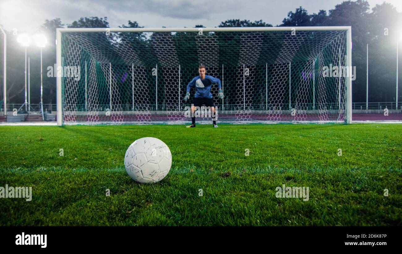 Tiro di una palla di calcio su un erba durante la penalità nel campionato. In background il portiere professionista si trova in obiettivi pronti a difendere. Foto Stock
