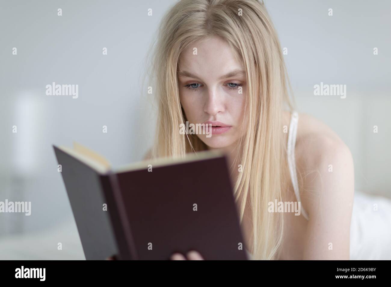 Donna giovane concentrata che legge un libro a letto durante la mattina. Foto Stock