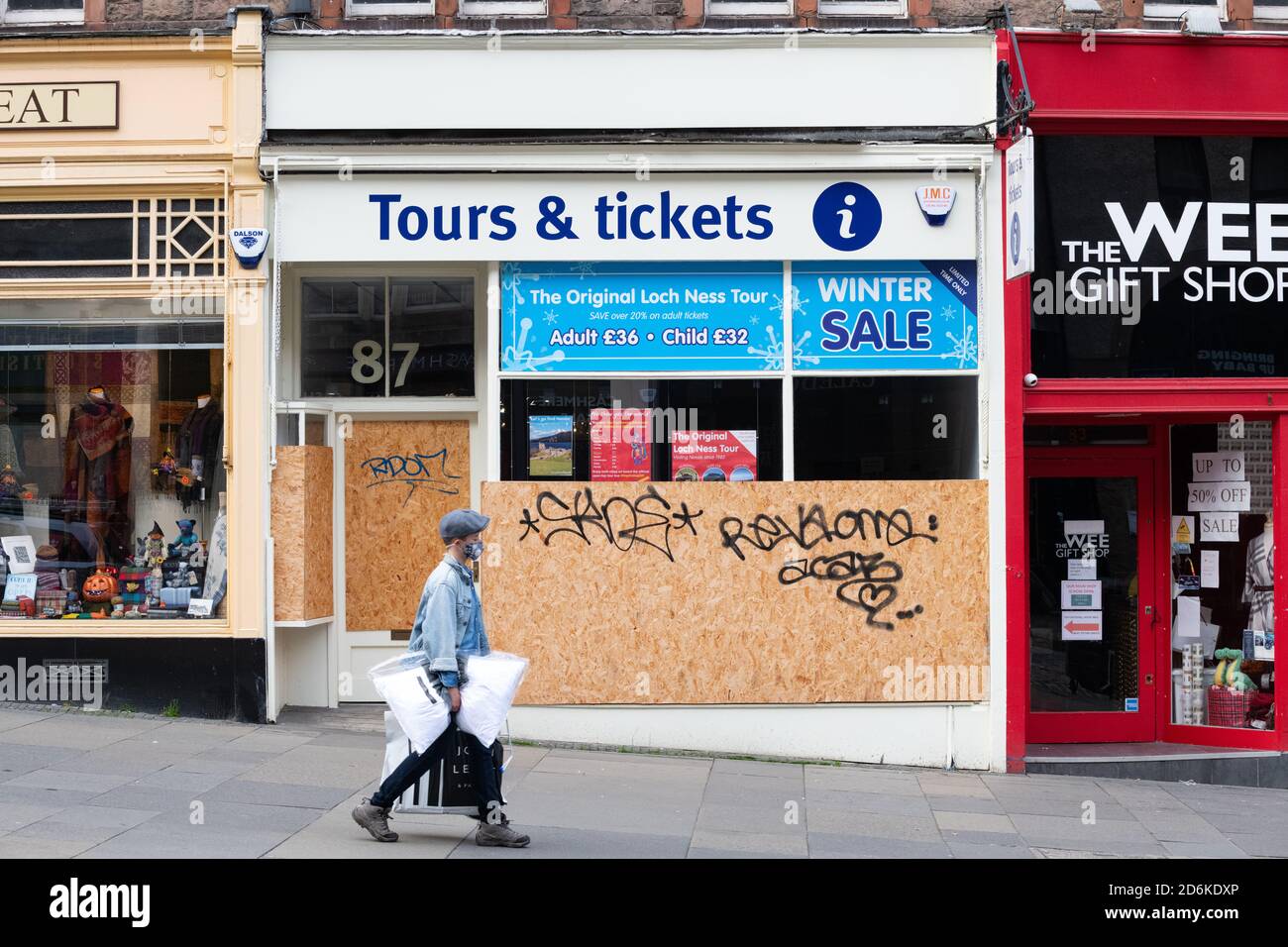 L'uomo che indossa la maschera per lo shopping a Edimburgo cammina oltre il tour aziendale imbarcato sul Royal Mile durante la pandemia del coronavirus, Scozia Foto Stock