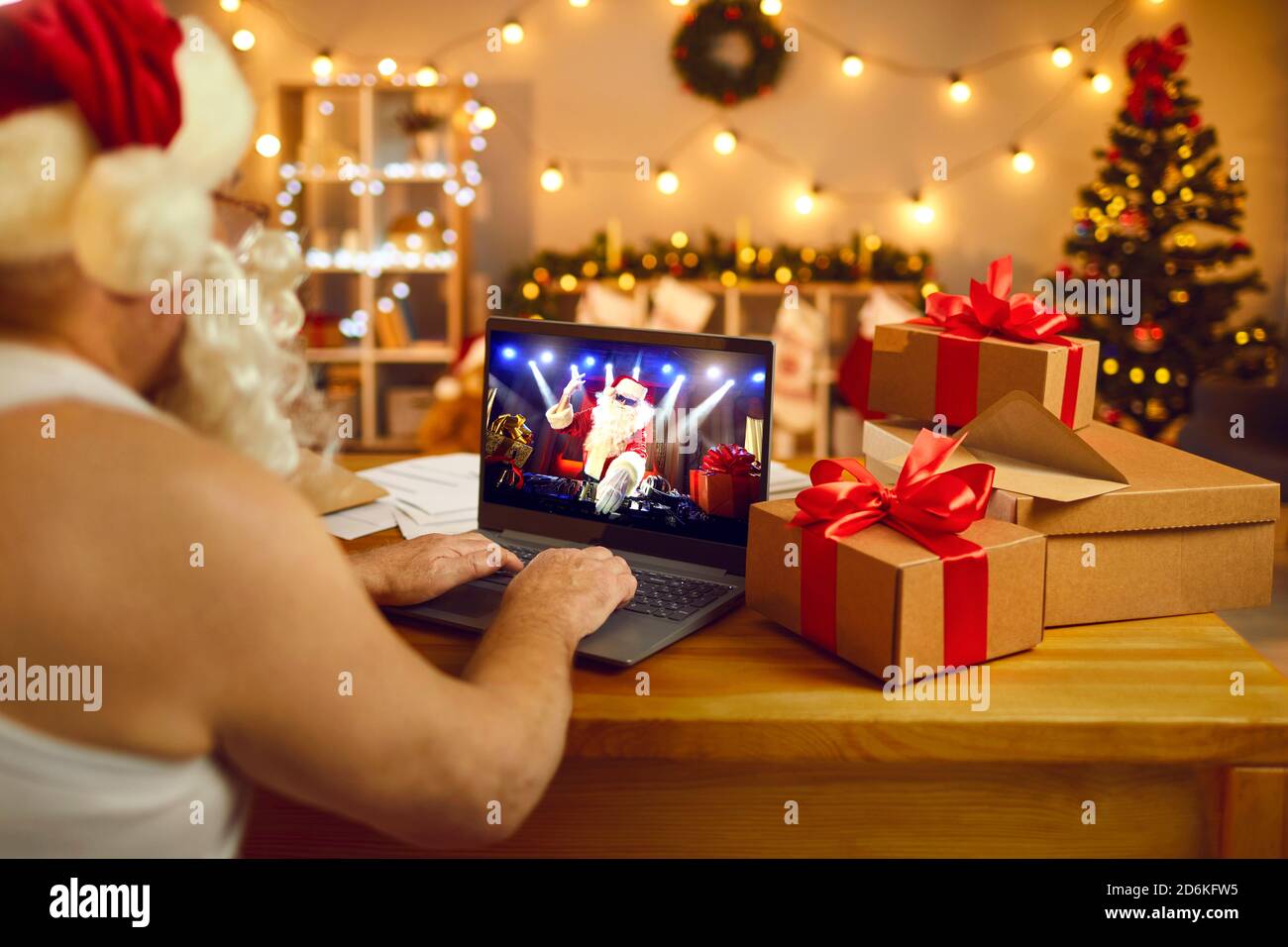 Padre Natale seduto alla scrivania con computer portatile guardando spettacolo dal vivo Con Babbo Natale DJ al divertente party notturno Foto Stock