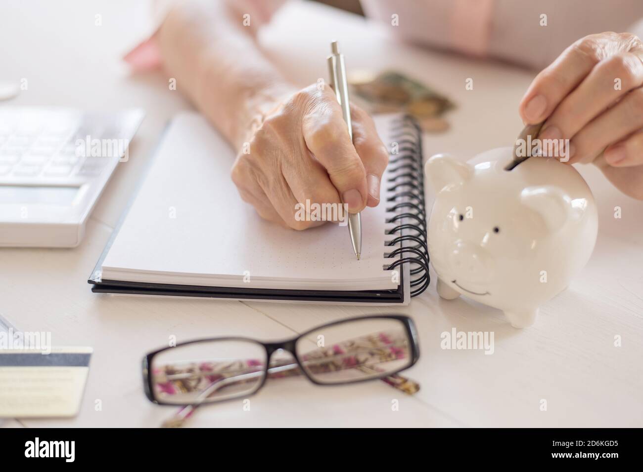 Le mani delle donne anziane contano la pensione e la mettono nella Banca piggy, il concetto di pensione, risparmio, vecchiaia. Foto Stock