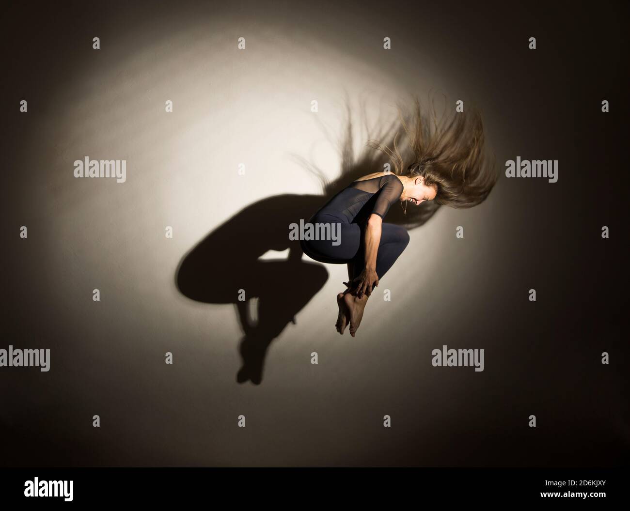 donna al buio esegue il salto ginnico, su uno sfondo bianco c'è un'ombra da una forma. Fotografia da studio. Foto Stock