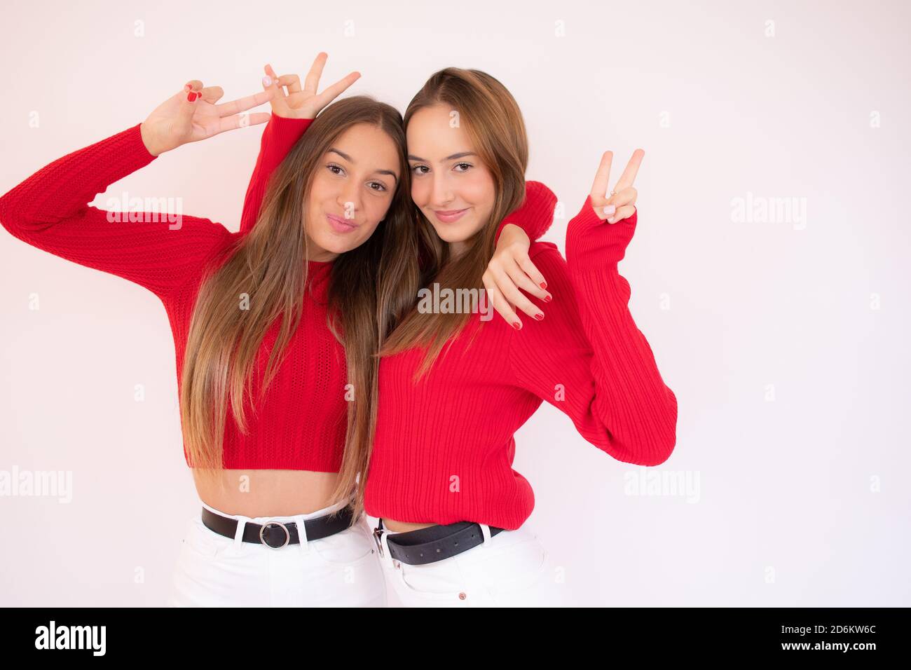 Foto di graziose due fidanzate che mostrano i simboli del segno a V che abbracciano indossando un pullover rosso e jeans isolato sfondo bianco Foto Stock