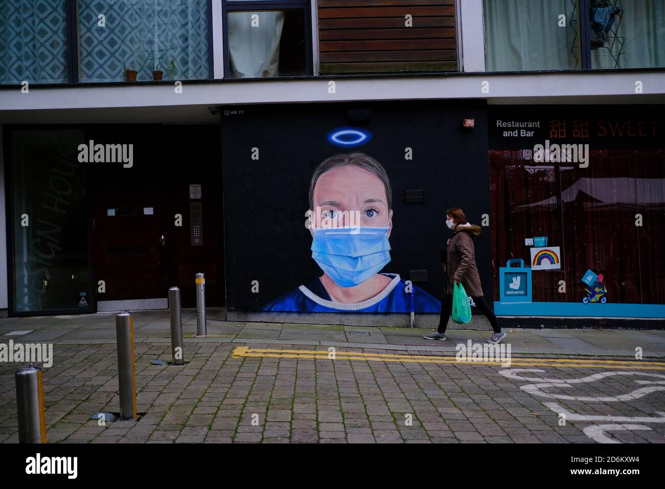 Donna in una maschera facciale che passa dal murale in High Street. Nurse Debra Williams come angelo di AKSE. Nuova arte di strada che celebra gli eroi NHS. Foto Stock