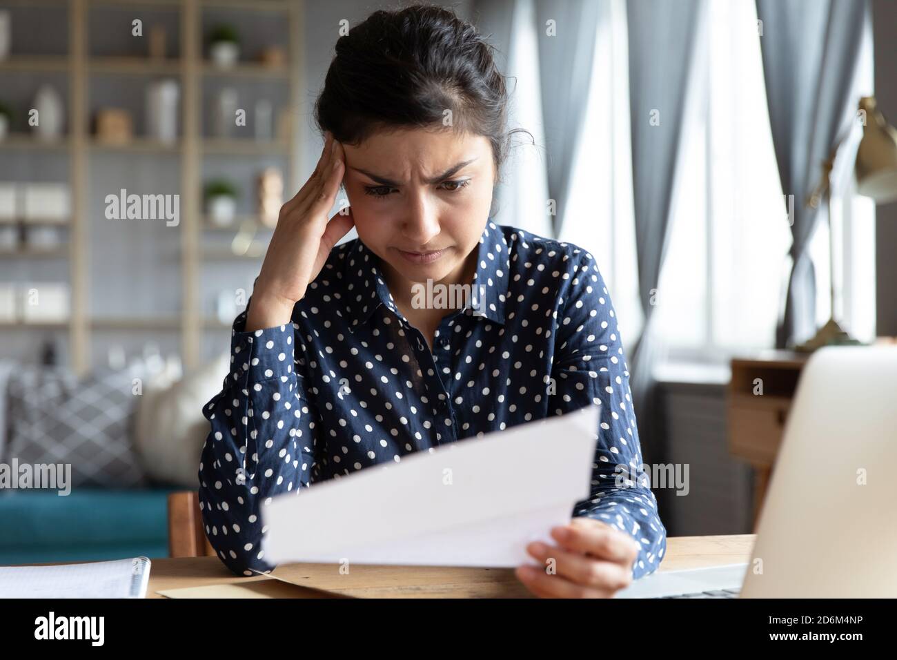 La donna di etnia indiana si siede alla scrivania leggendo la lettera si sente delusa Foto Stock