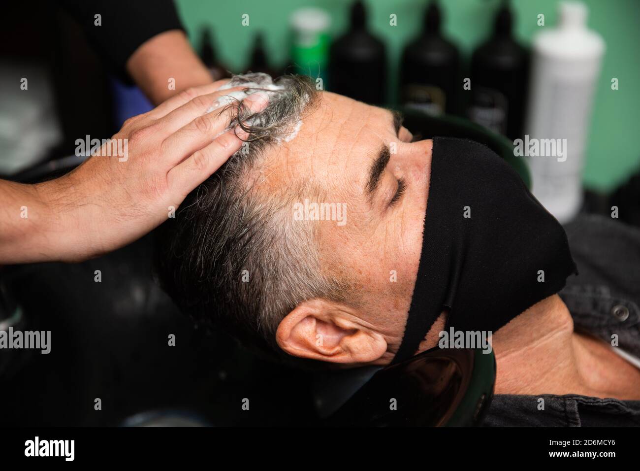 Uomo caucasico bianco con maschera nera di protezione coronavirus pandemico  è sdraiato mentre alcune mani del barbiere si lavano i capelli con acqua e  sapone in ha Foto stock - Alamy