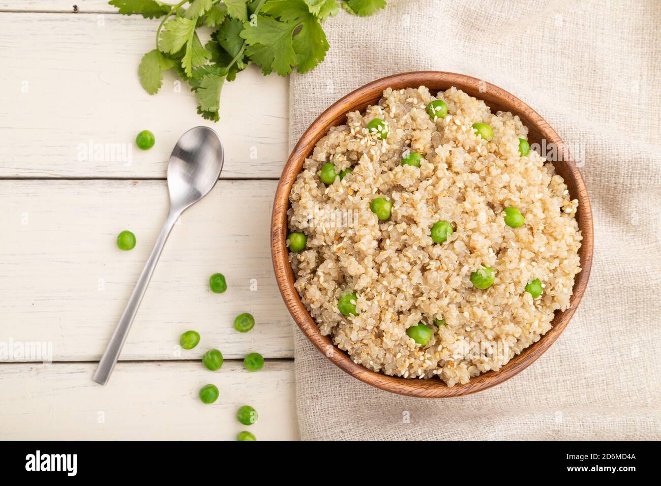 Porridge di quinoa con piselli verdi in ciotola di legno su fondo di legno bianco e tessuto di lino. Vista dall'alto, disposizione piatta, primo piano. Foto Stock