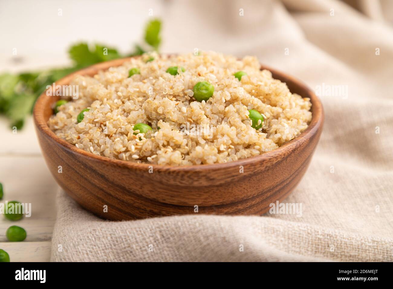 Porridge di quinoa con piselli verdi in ciotola di legno su fondo di legno bianco e tessuto di lino. Vista laterale, primo piano, messa a fuoco selettiva. Foto Stock