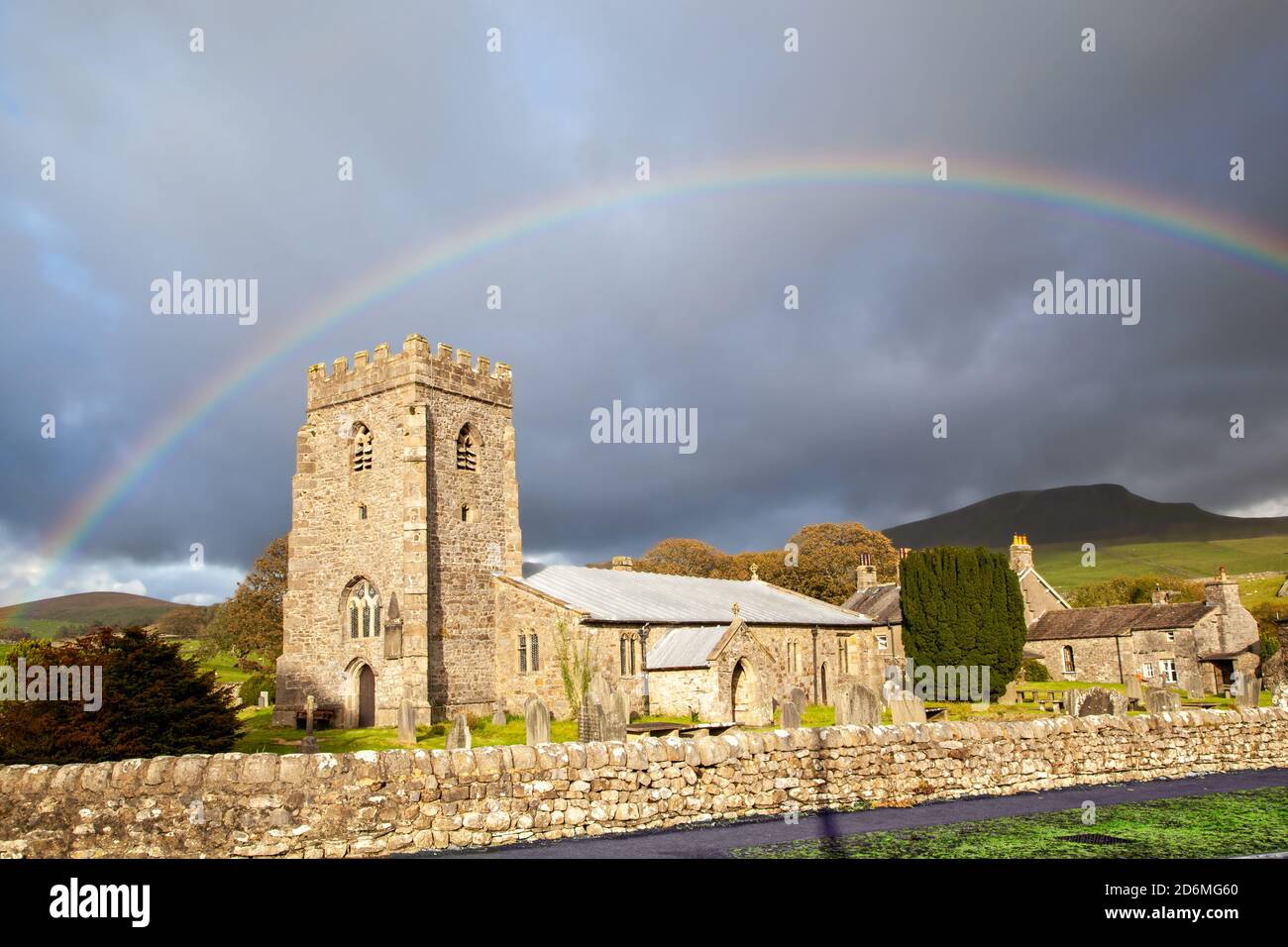Arcobaleno sopra la chiesa del villaggio di St Oswalds nel Yorkshire villaggio di Horton in Ribblesdale con la montagna di Pen-y-gand sulla Via Pennina Foto Stock