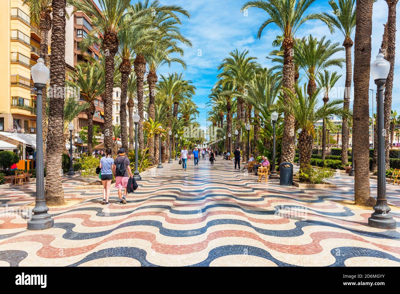 Persone che camminano su una passeggiata costeggiata da palme ad Alicante, Spagna. Alicante è una città situata a sud-est della penisola iberica. Foto Stock
