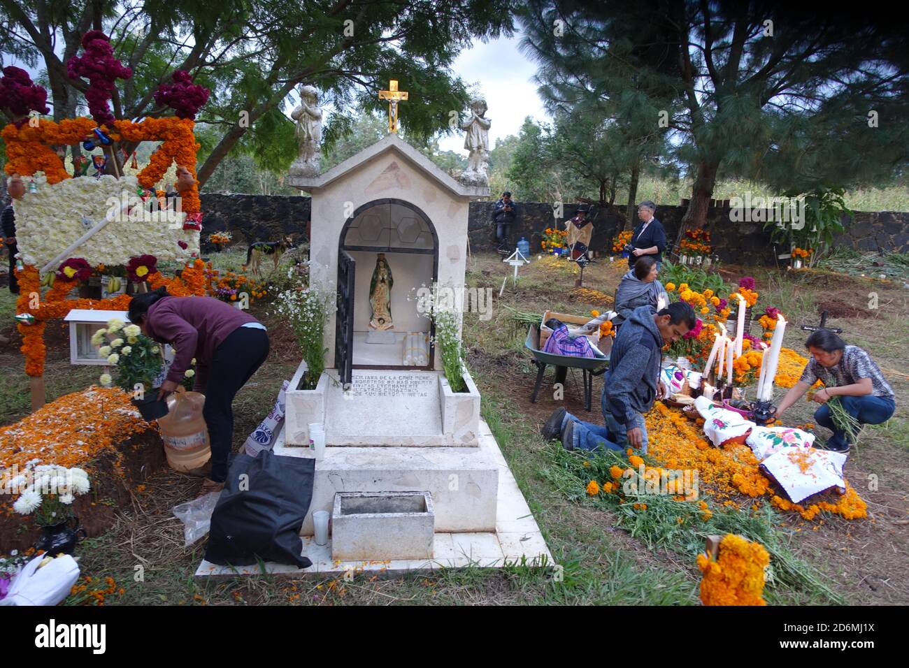 Le famiglie decorano tombe a Patzcuaro, in Messico, durante il giorno dei morti, con i tradizionali marigolds, oltre a cibi e altri piatti preferiti dei loro cari. Foto Stock