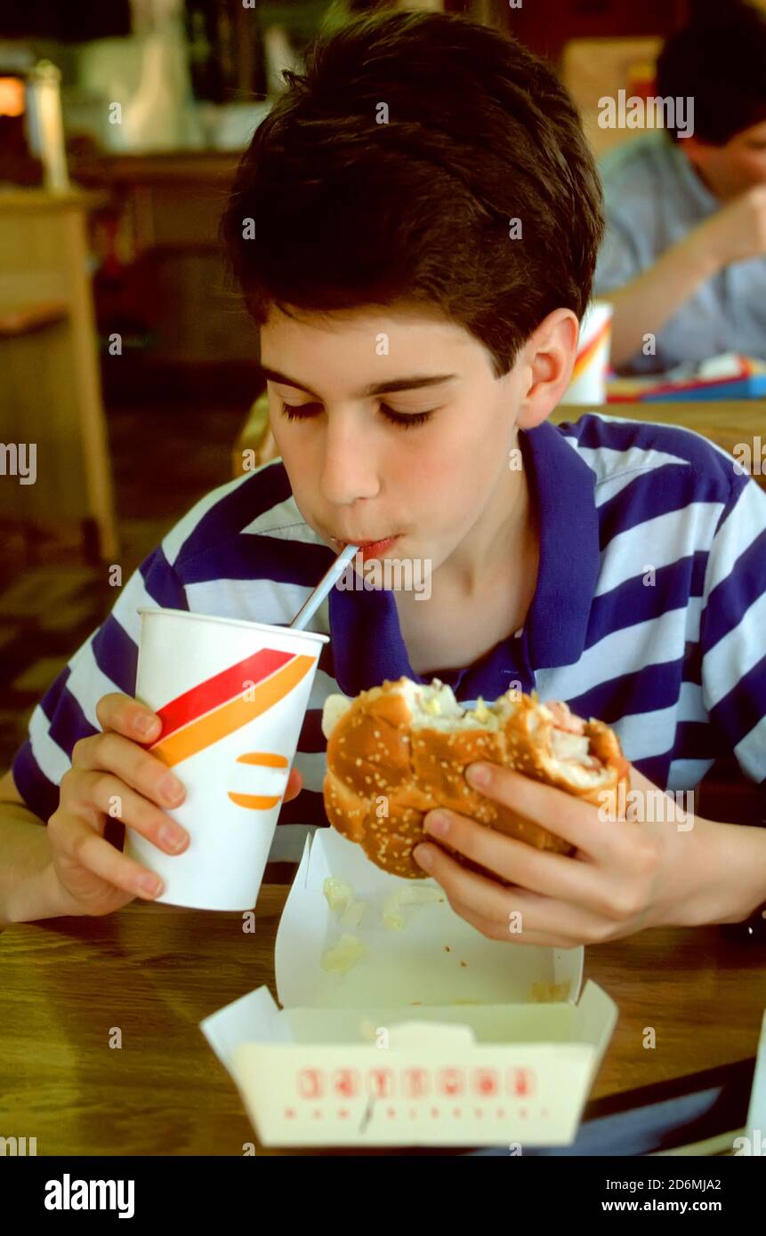 14 anni maschio bianco mangia un grande hamberger a. un ristorante fast food Foto Stock