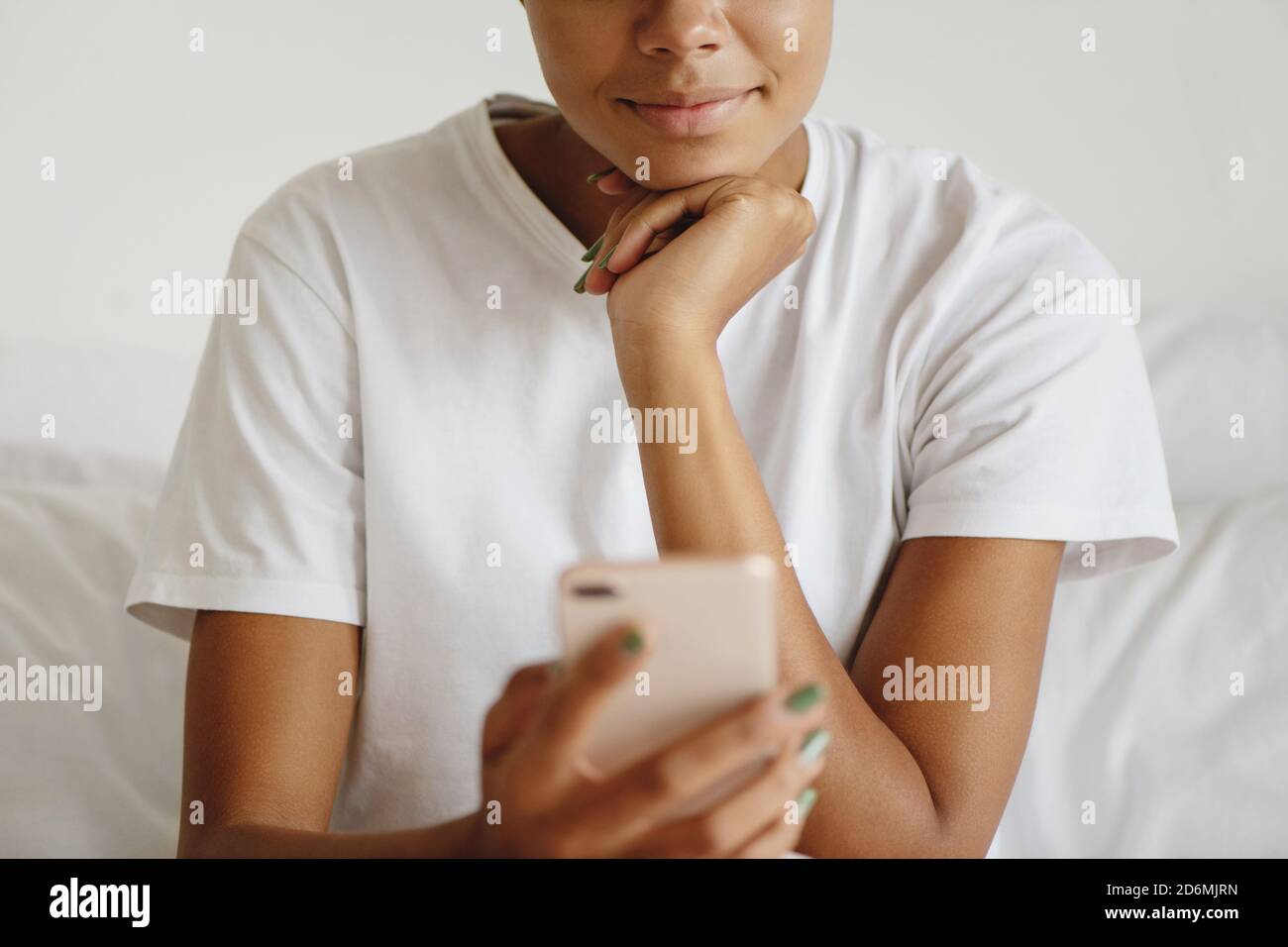 Foto ritagliata di giovane attraente donna africana che guarda il display del telefono cellulare. Foto Stock