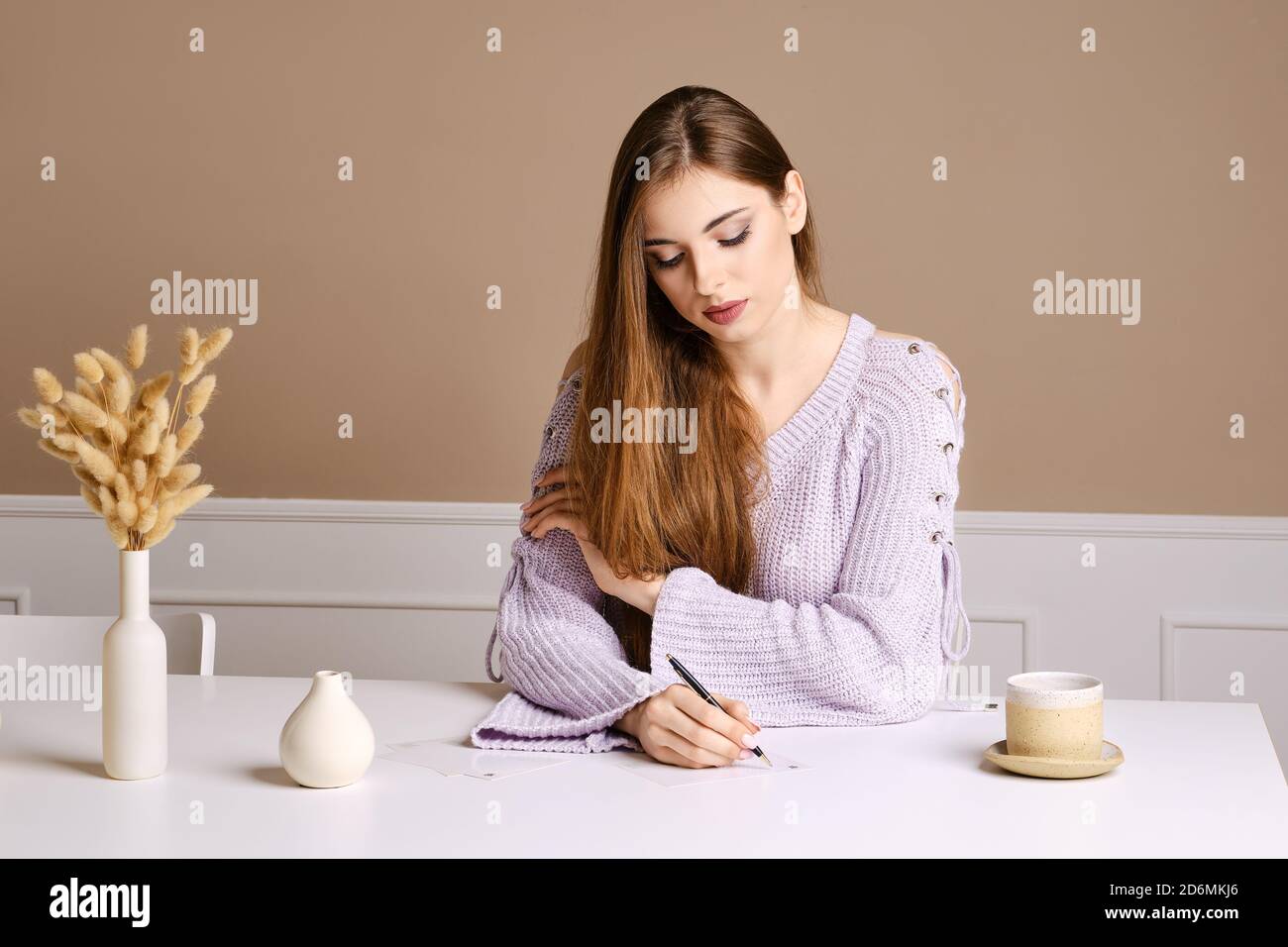 Gentile giovane donna si siede dietro il tavolo e segni saluto cartolina Foto Stock