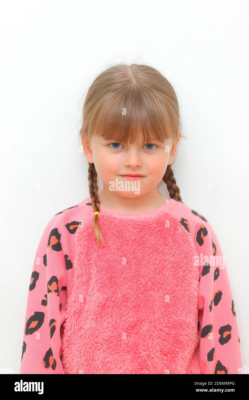Una bambina di 5 anni con i pigtail e un'espressione vuota sul viso contro uno sfondo bianco. Foto Stock