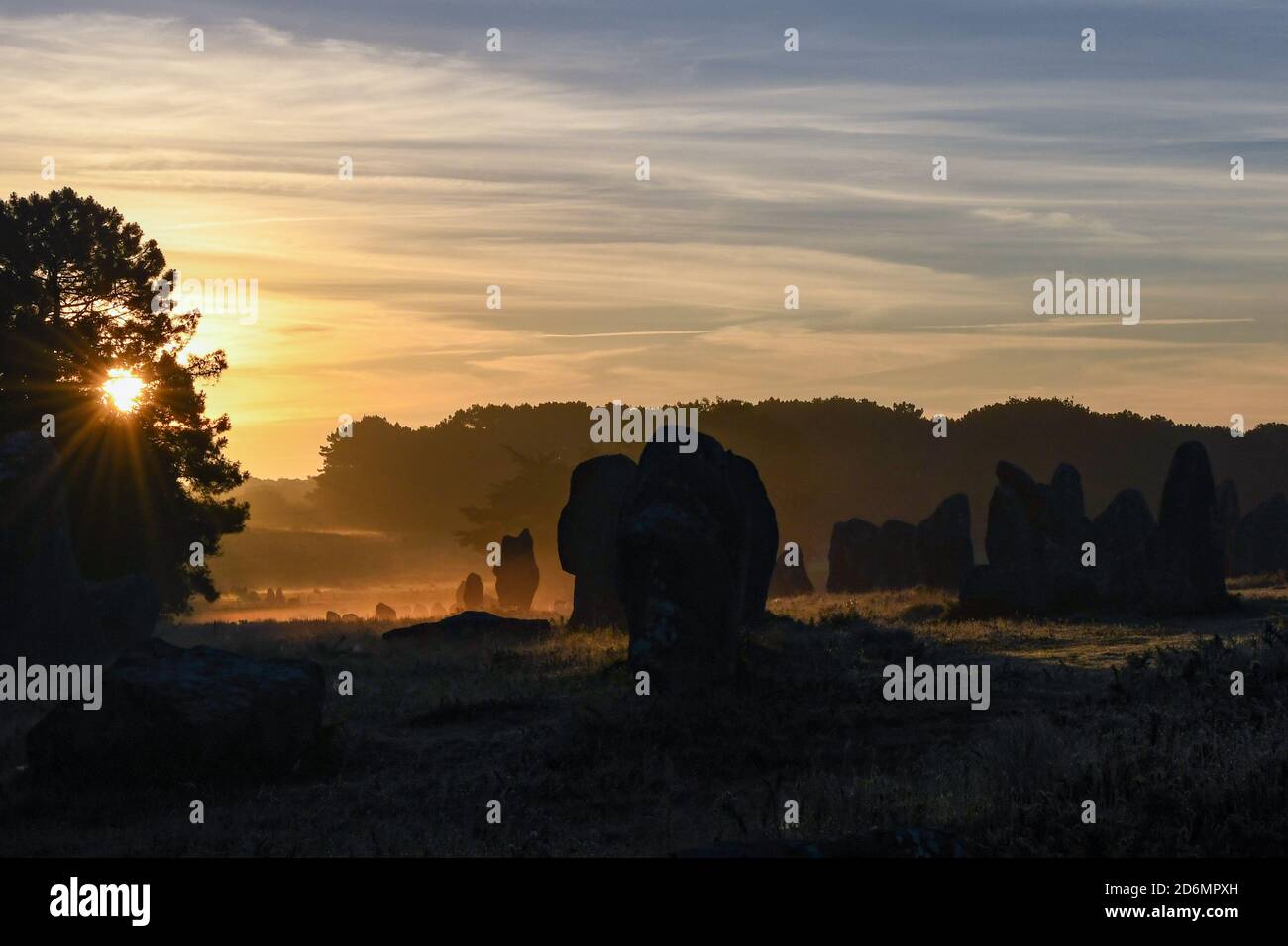 Alba che splende attraverso le corsie di allineamenti in pietra, Carnac, Bretagna, Francia Foto Stock