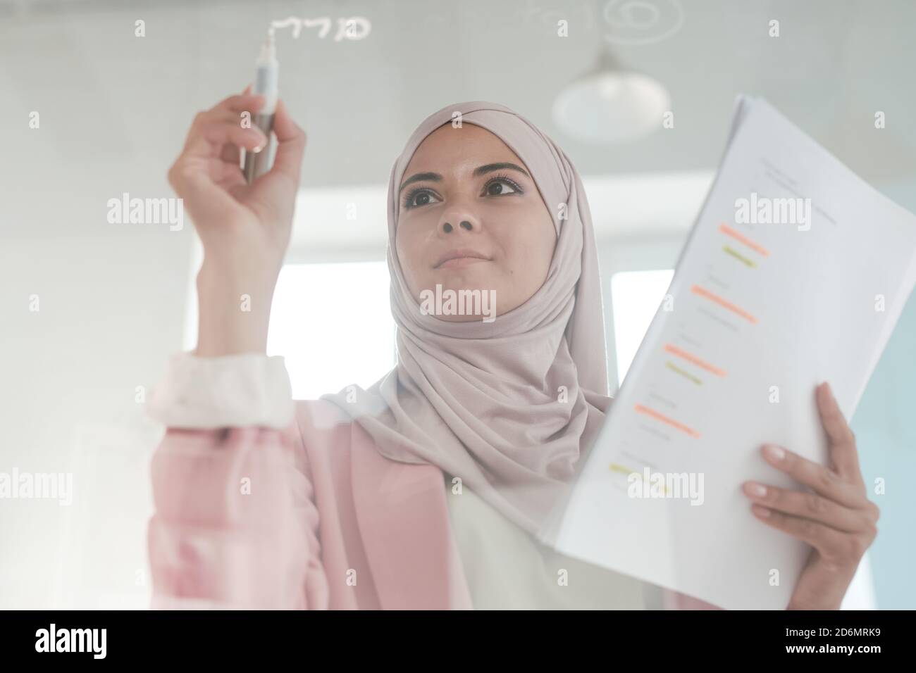 Giovane serio broker femminile in hijab tenendo documenti finanziari e. evidenziatore Foto Stock