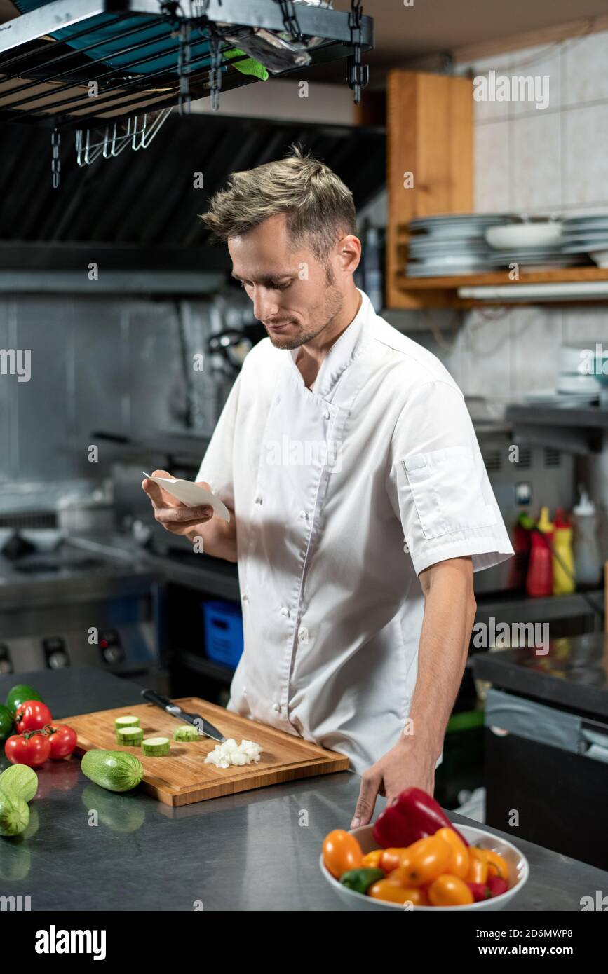 Giovane chef professionista contemporaneo che guarda attraverso la lista degli ingredienti Foto Stock