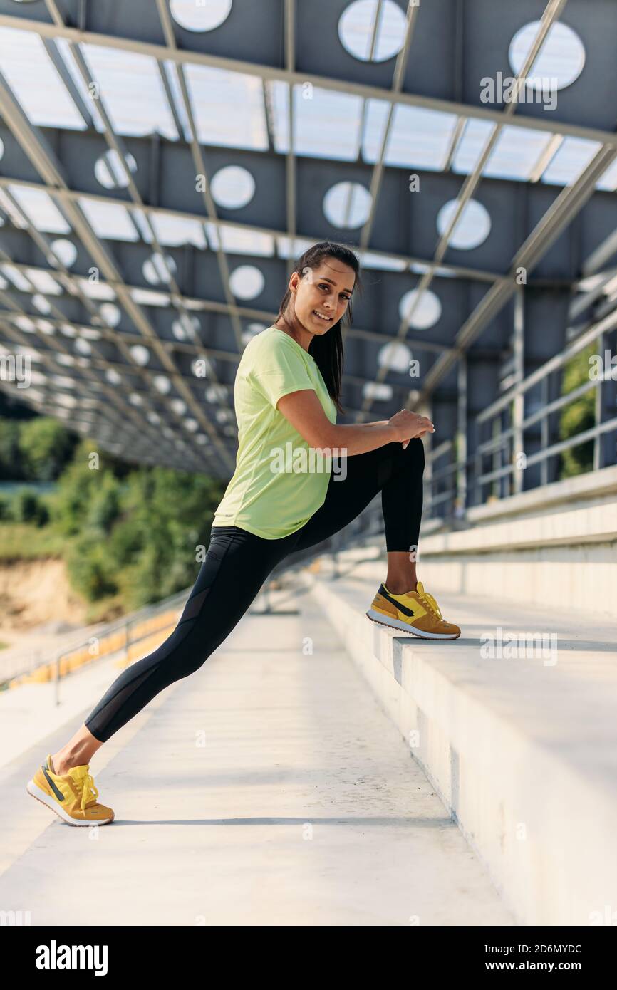 Donna positiva in abbigliamento sportivo che si allunga per le gambe sui gradini Foto Stock