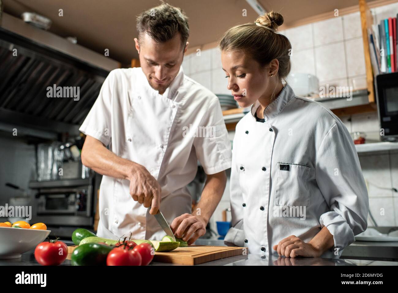 Giovane chef professionista con coltello che mostra al suo apprendista come fare cuocere le zucchine Foto Stock