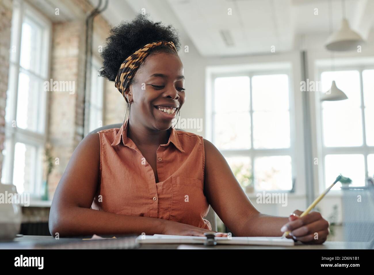 Felice giovane donna di etnia africana che prende appunti in copybook per tabella Foto Stock