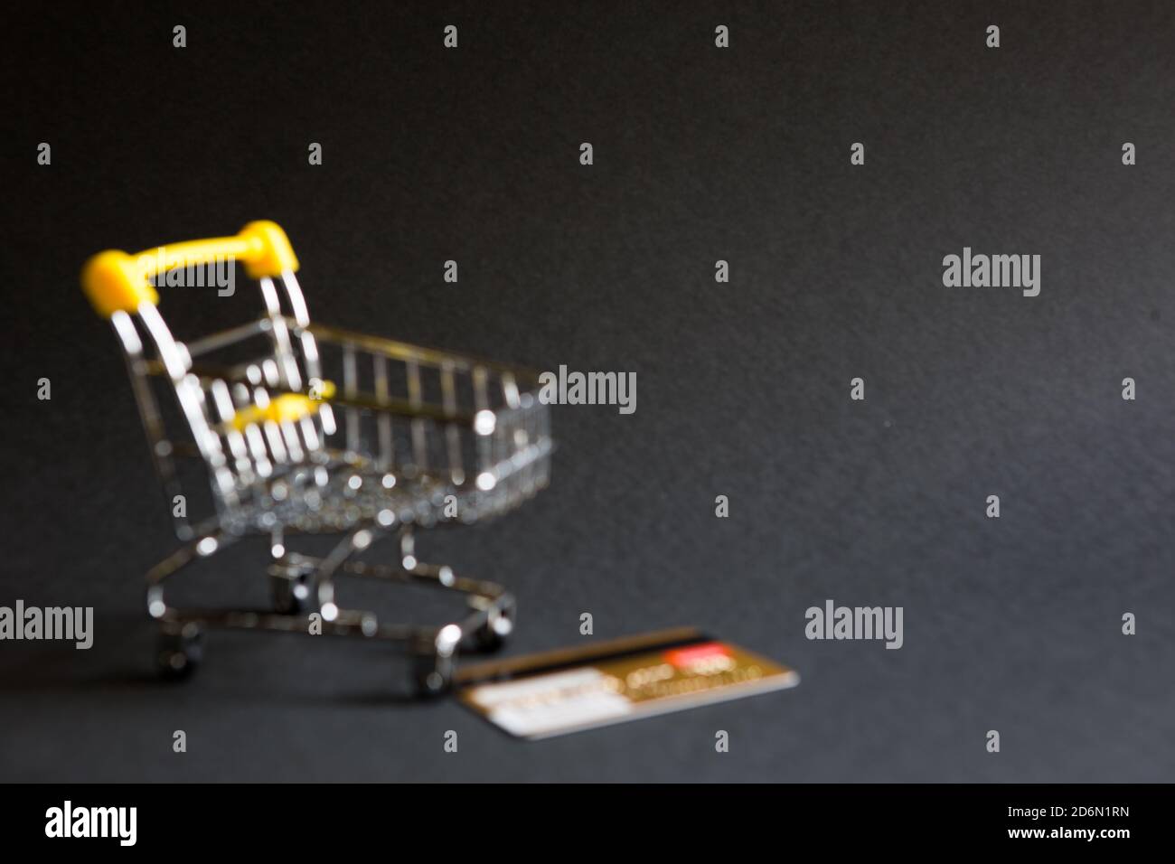 Defocalizzare il carrello vuoto della spesa da un supermercato e carta di credito oro di plastica Banca su sfondo nero. Black Friday, carrello, shopping, online Foto Stock