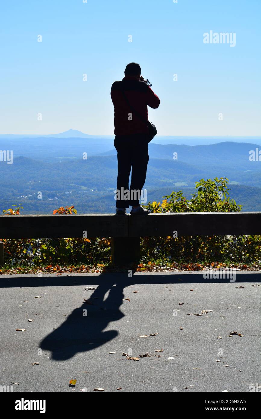 Un uomo si erge sulla ringhiera per scattare foto in un punto panoramico sulla Blue Ridge Parkway, nella Carolina del Nord. Foto Stock