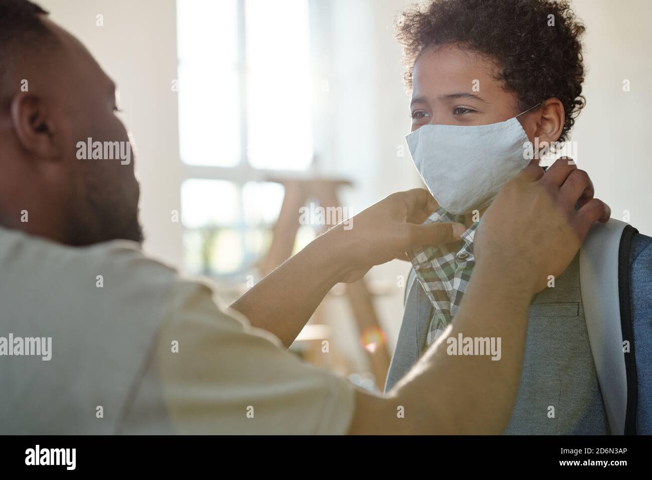 Giovane padre che raddrizza il collare della camicia del suo figlio con protettivo maschera sulla faccia Foto Stock