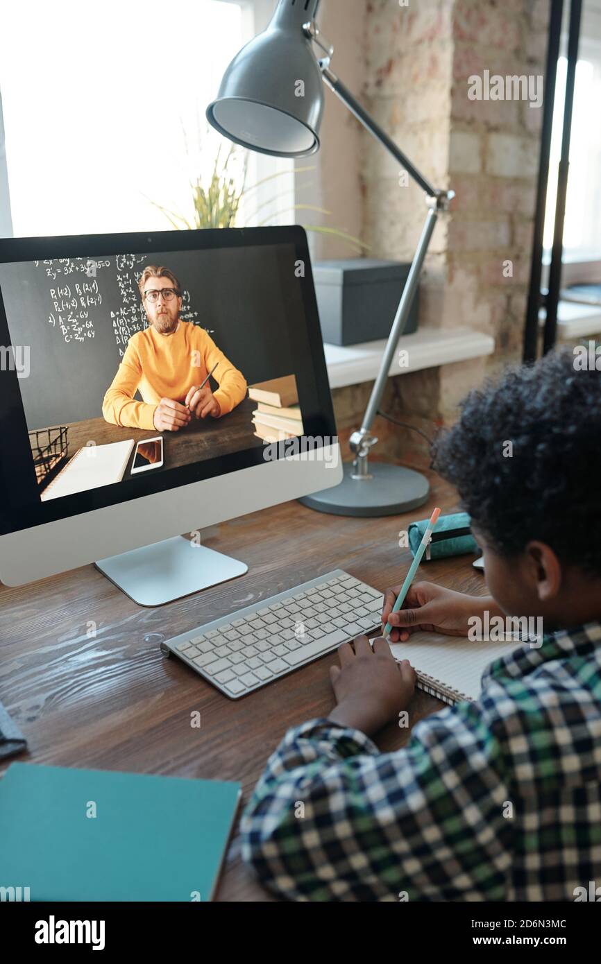 Piccolo scolaro che ascolta il suo insegnante sullo schermo del computer e. prendere appunti Foto Stock