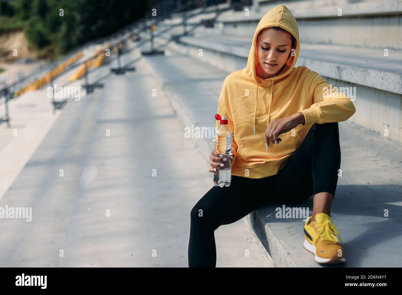 Atleta femminile in felpa con cappuccio gialla che si rilassa sui gradini Foto Stock