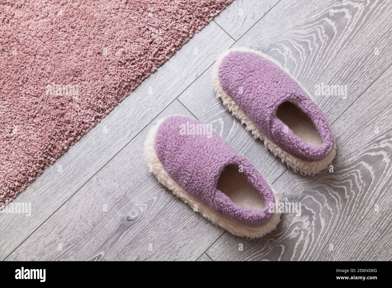 Le comode pantofole in lana si trovano su un pavimento in legno grigio vicino al rosa moquette Foto Stock