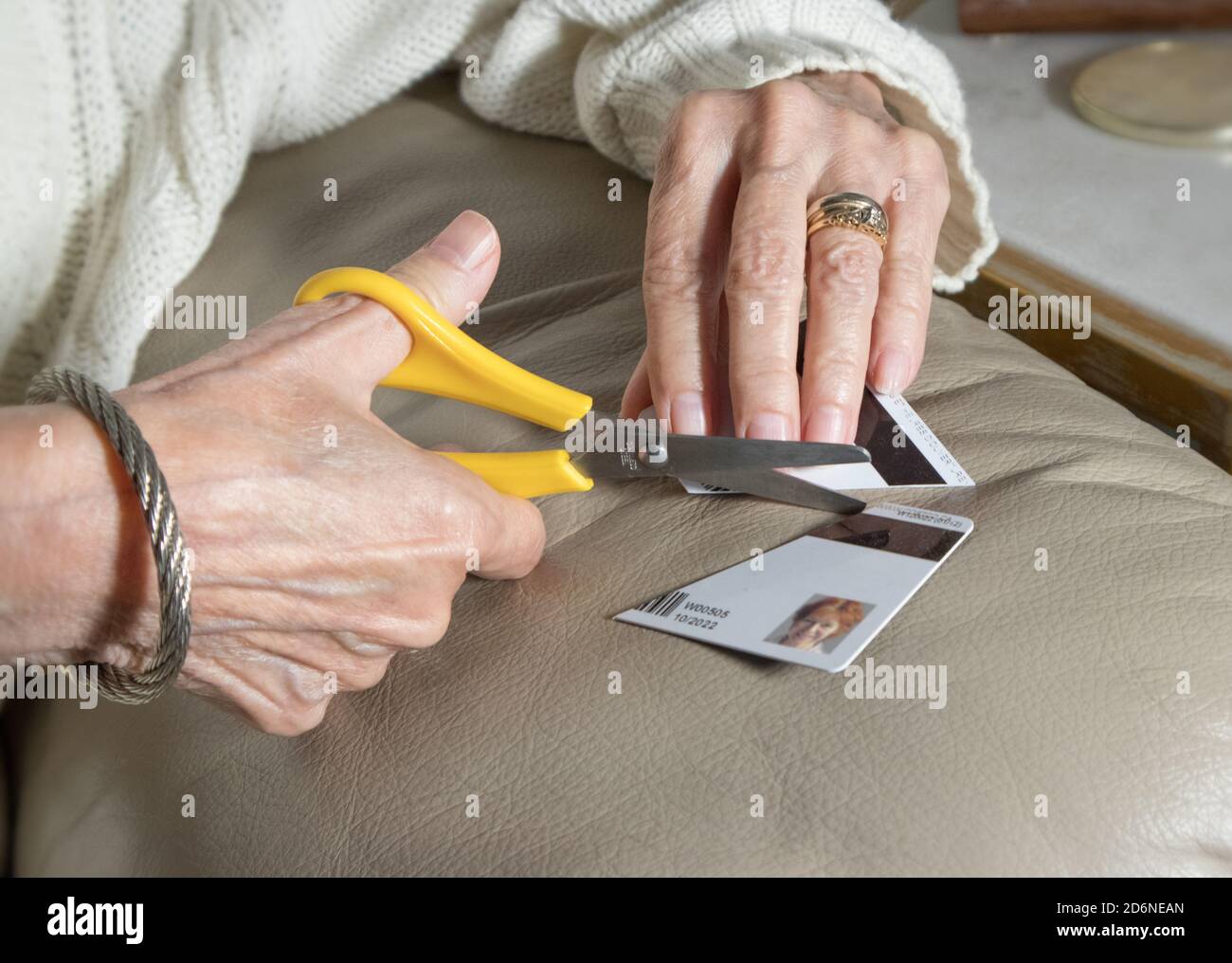 Le mani di una donna matura che taglia una carta (di credito) con forbici. Foto Stock