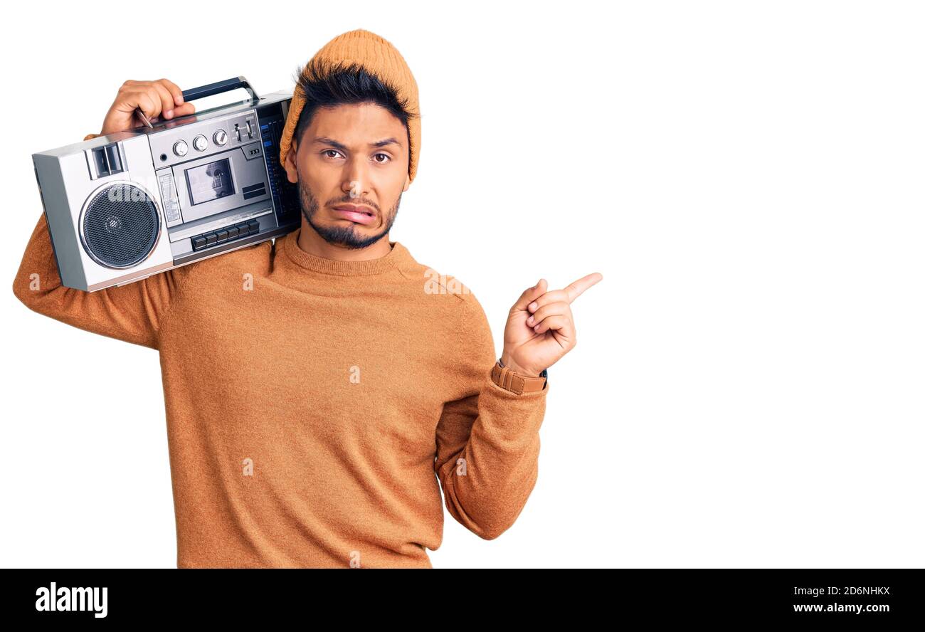 Bel giovane latino-americano che tiene il boombox, ascoltando la musica che punta da parte preoccupato e nervoso con l'indice, preoccupato e sorpreso expr Foto Stock