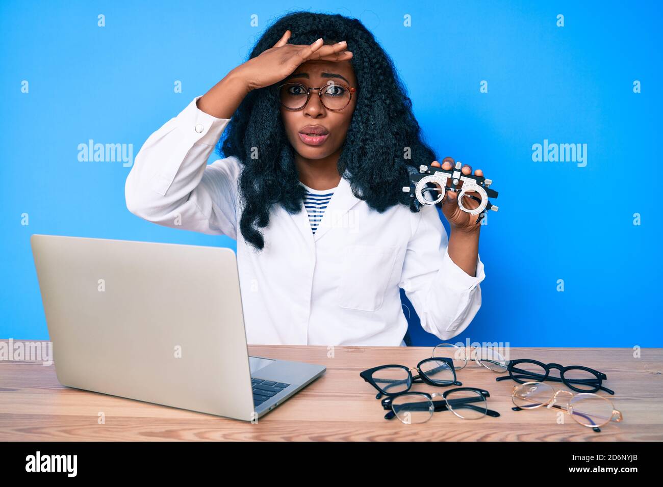 Bella donna africana che tiene occhiali di optometria stressati e frustrati con la mano sulla testa, sorpresa e faccia arrabbiata Foto Stock