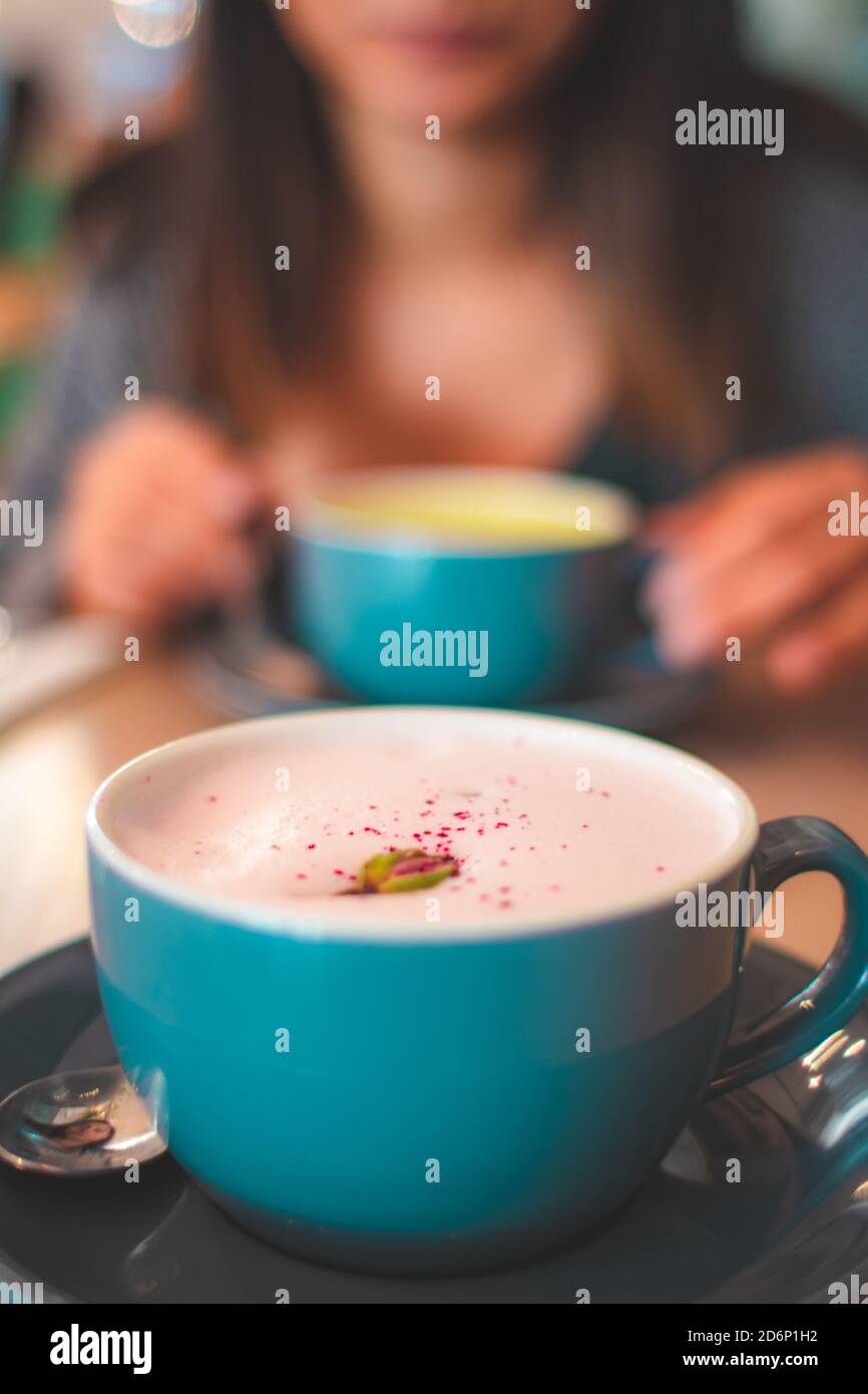 Primo piano su un caffè cremoso di latte di rose con petali in una tazza blu e donna sullo sfondo Foto Stock