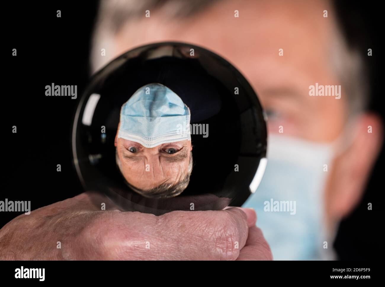 Uomo anziano indossando maschera contro il coronavirus e riflesso in fortuna dicendo palla di vetro. Concetto di persone che scelgono la responsabilità nelle elezioni Foto Stock