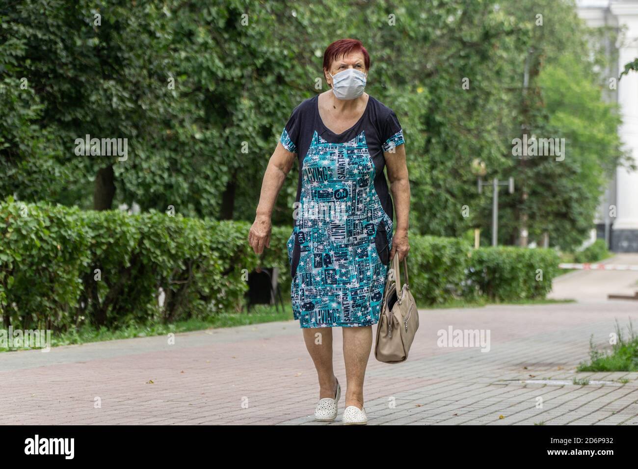 Donna anziana solitaria che indossa una maschera medica protettiva che cammina lungo la strada in città. La sopravvivenza degli anziani durante la pandemia. Foto Stock