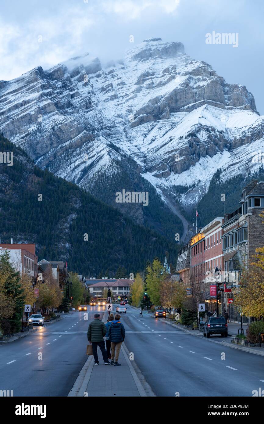 Vista sulla strada di Banff Avenue in autunno e in inverno di notte. Montagna Cascade innevata sullo sfondo. Banff, Alberta, Canada Foto Stock