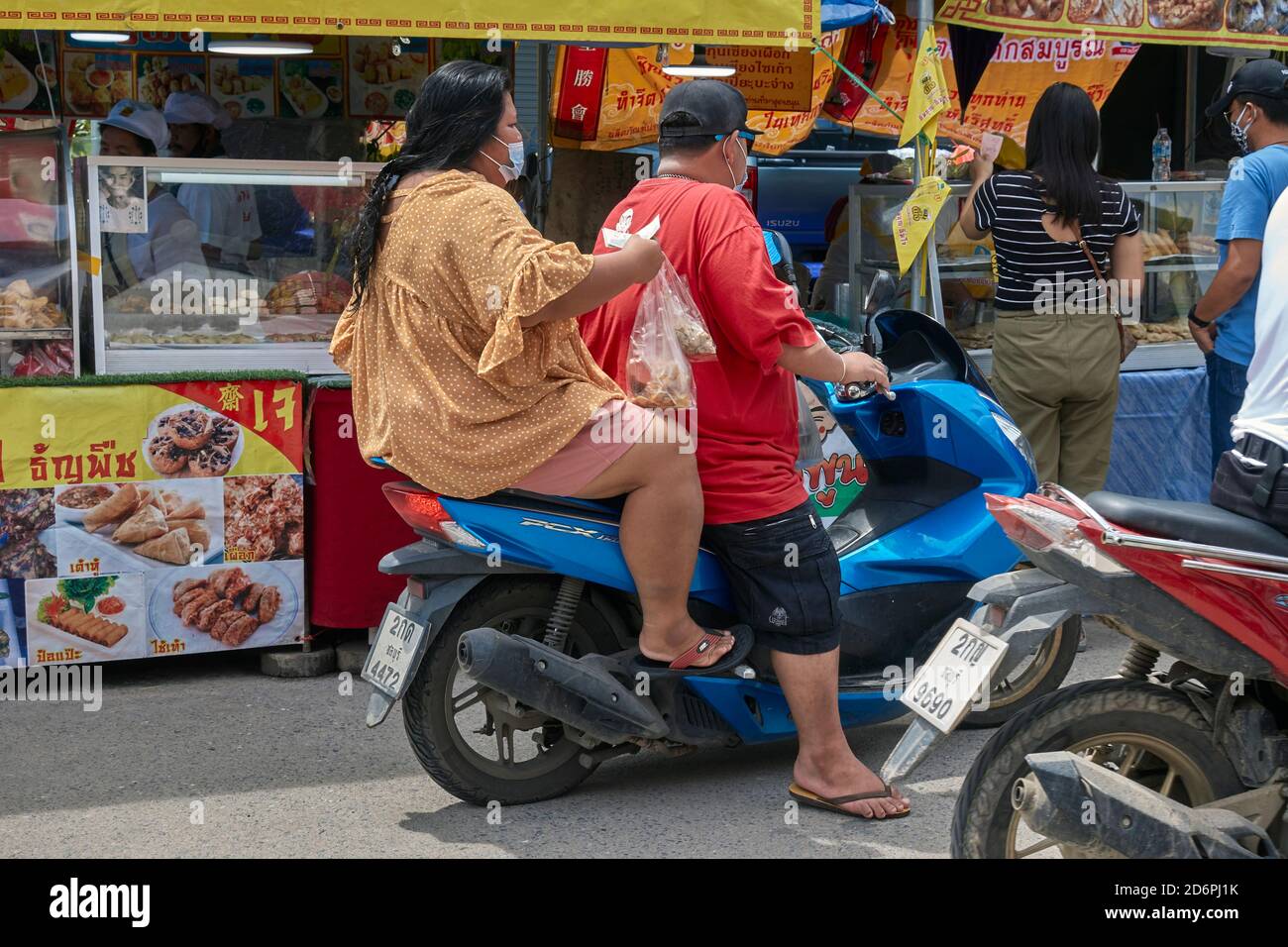 Coppia obese che cavalcano una motocicletta attraverso un mercato alimentare di strada avendo raccolto cibo in una bancarella. Thailandia Foto Stock