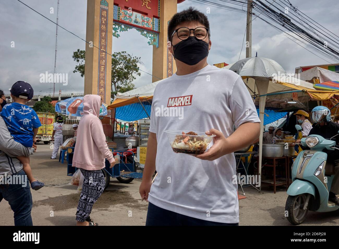Uomo con un piatto di cibo da asporto che cammina attraverso un mercato alimentare di strada. Thailandia Sud-est asiatico Foto Stock