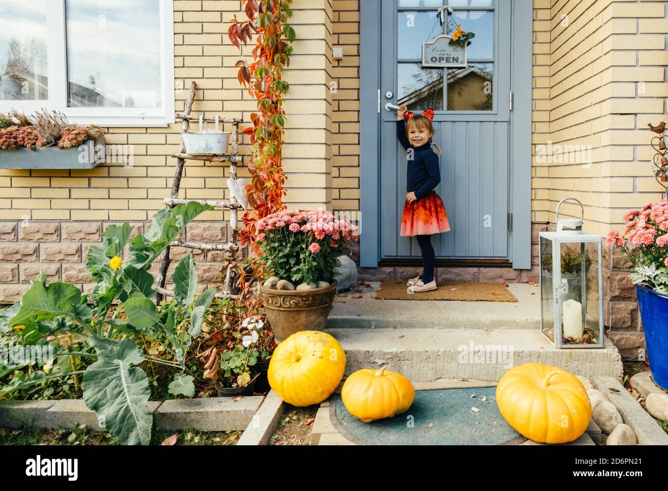 Giovane ragazza carina sulla casa di campagna portico con zucche in cappelli costumer. Halloween felice. Halloween bambini. Foto Stock